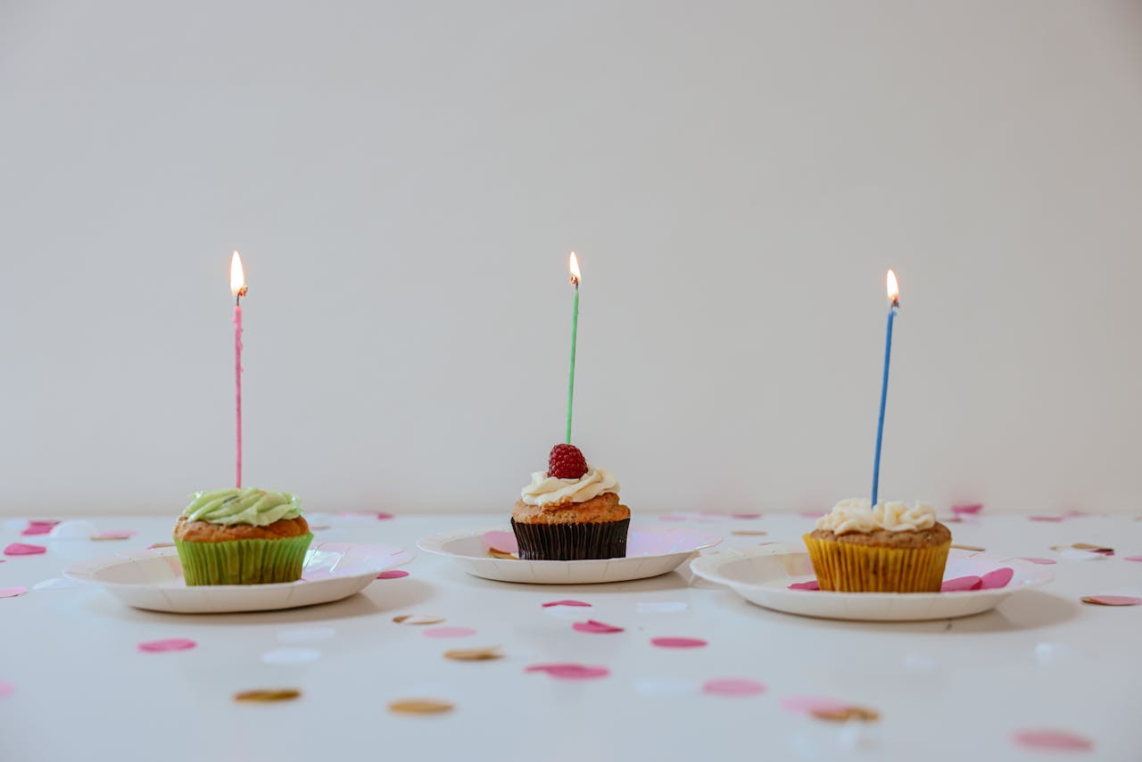 A festive arrangement of cupcakes with lit candles surrounded by confetti for a cheerful birthday celebration.